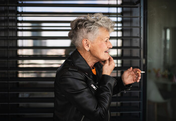 Portrait of senior woman with cigarette standing against black backround, relaxing.