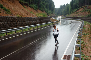 Woman with yellow backpack walking on wet road among mountains