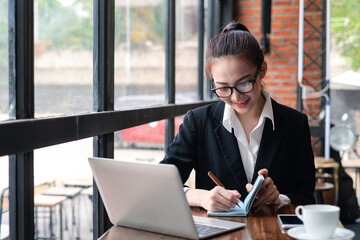 Young Asian businesswoman wearing glasses is taking notes on a laptop at the office.