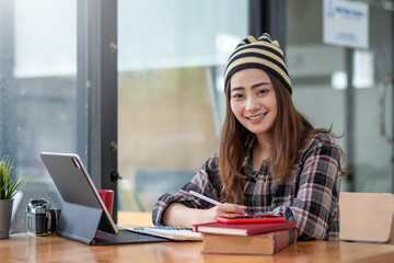 Young Asian woman wearing a balaclava sitting at work using a taking note tablet. Looking at the camera.