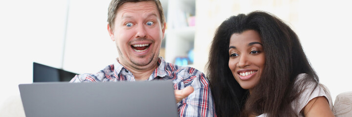 Young man and woman are sitting in front of laptop screen and smiling
