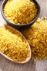 Composition with a bowl and spoon of uncooked bulgur on a table