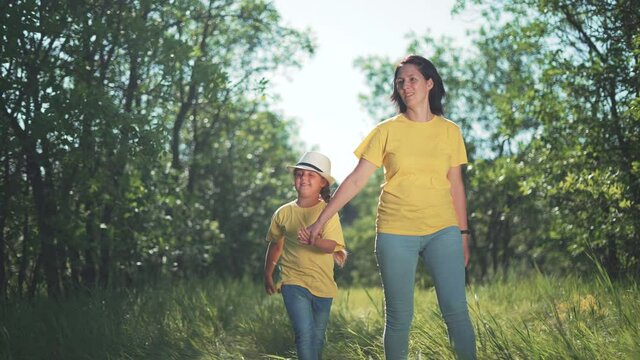 Happy family. Mom and daughter in forest park. People walk on grass. Happy team mom and daughter. Family is walk on grass in park. People walk along the tava in forest. Happy family concept