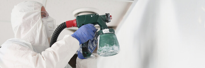 Construction worker in protective suit and respirator painting wall with spray gun
