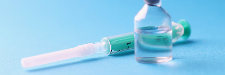 Closeup of glass jar with medicine and sterile syringe on blue background