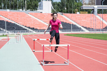 Obraz premium Woman athlete jumping over an obstacle. Running with hurdles. Active lifestyle
