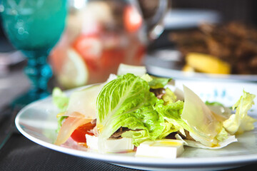 Healthy eating scene. Close up of gourmet delicious salad with fresh lettuce, cherry tomatoes and cheese on a white plate. Front view, selective focus.
