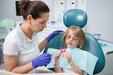 Female dentist showing removable dental plate to her little patient