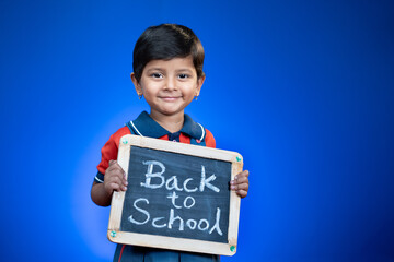 Happy smiling Indian school kid holding back to school sign board on blue background