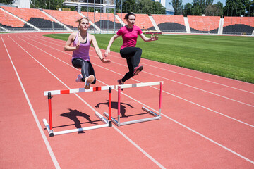 Fototapeta premium Two female sportswomen are jumping over an obstacle. Running with hurdles. Active lifestyle