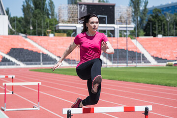 Obraz premium Woman athlete jumping over an obstacle. Running with hurdles. Active lifestyle