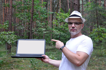 Obraz premium Young handsome man with a computer in the forest.