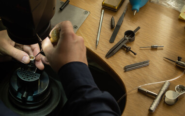 Close-up of goldsmith hand decorating precious ring with beautiful gemstones. Professional jeweler...