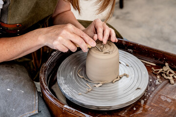 Woman working on the potter's wheel. Ceramist young woman making clay product on pottery lathe in studio. Close up of female hands working on potters wheel