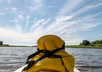 landscape with a river, in the foreground a sup board with a yellow, waterproof rubber bag