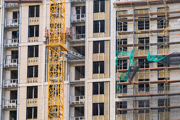 Fototapeta premium metallic crane machinery attachment at windows of new residential building construction site. Exterior passive house wall heat insulation with mineral wool. Insulation facade of residential building