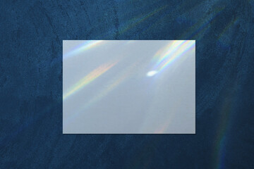 Empty white horizontal rectangle a4 poster, business card, flyer mockup with overlay of rainbow light refraction caustic effect and shadow on trendy dark blue concrete background.