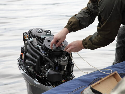 Boater hand start an broken outboard boat motor without the hood cap on the transom of the boat, emergency engine start with rope