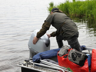 Boater man hands removes the hood of a 50 hp four stroke outboard motor on transom of boat, repair...
