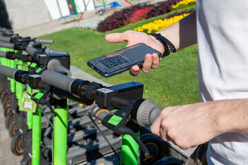 A young man rents an electric scooter by scanning the QR code with a smartphone