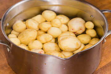 Stainless steel pot with raw young potatoes in water
