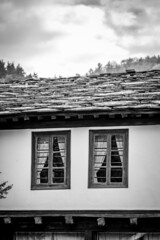 Smiling face look alike black and white perspective of old house in Bulgaria. Stone tiles roof and typical curtains on the authentic wooden frame windows.