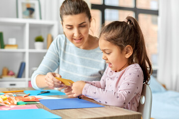 family, art and craft concept - mother spending time with her little daughter with glue making applique of color paper at home