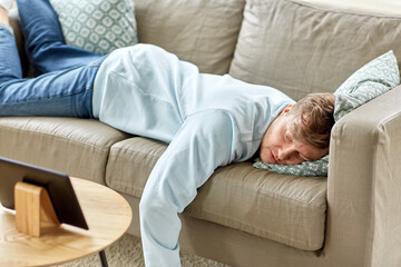 people, boredom and depression concept - bored or lazy young man with tablet pc computer lying on sofa at home