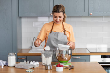 culinary, baking and people concept - happy smiling young woman cooking food on kitchen at home and sifting flour through sieve