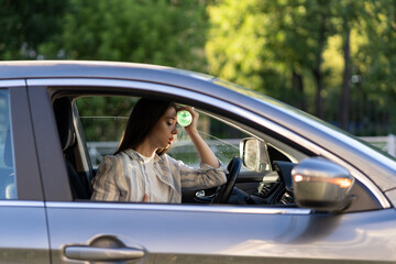 Fototapeta na wymiar Exhausted woman driver feeling headache, sitting inside her car, applies bottle of water to forehead, hot weather. Tired girl stop after driving car in traffic jam. Blood pressure, heat concept. 