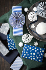 Obraz premium Christmas composition in white ,green and blue shades, Christmas balls and candle, gift boxes and snowflakes, decorative white spruce branches and snowball on a green tablecloth, top view