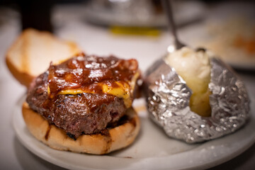 A juicy and tasty burger with crispy bacon and melted cheese and dripping sauce and a roasted potato on the side