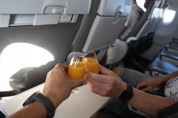 Two hands toast with glasses of orange juice on a plane trip.