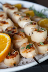 Grilled scallops on wooden skewers with orange and fresh thyme.