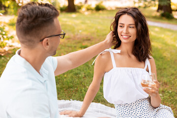 leisure and people concept - happy couple with drinks and food having picnic at summer park