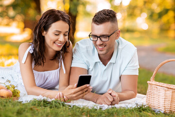 leisure and people concept - happy couple with smartphone having picnic at summer park