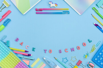 Frame made of colorful school and office stationery on blue background with copy space. Pencil case, calculator, unicorn, pens and pencils, stitches and curly paper clips. Preschool Education concept.