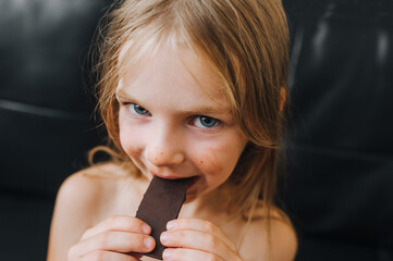 Portrait of a funny little red-haired girl, a child, who is smeared in black, milk chocolate and...