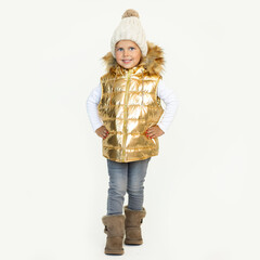 Children's fashion. Photo of little girl in warm natural wool hat gold vest coat kids hood, waistcoat in Winter boots in CHESTNUT color, Fluff Mini Quilted Sheepskin. Studio shot on white background