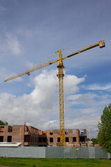 Yellow tower crane on the construction of a modern multi-storey building. A tower crane is working on the construction of a brick residential building.