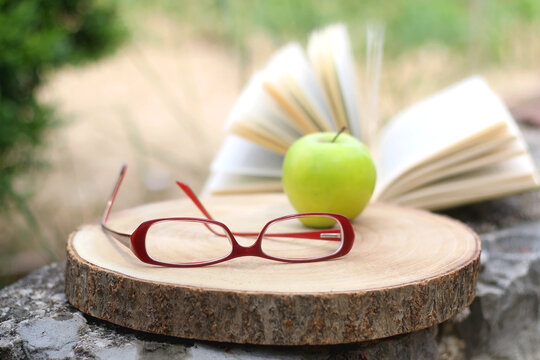 Red reading glasses, green apple and open book. Selective focus. - Powered by Adobe