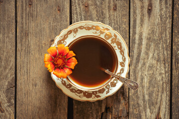 a cup of coffee with one red flower on handles on a wooden background, coffee