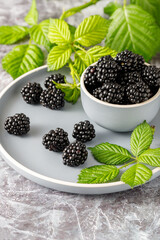 Ceramic blue bowl of fresh picked ripe blackberries, branch with leaves on plate over vintage stone