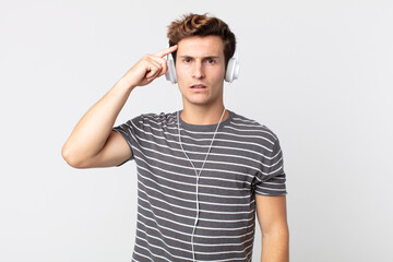 young handsome man feeling confused and puzzled, showing you are insane. listening music concept