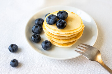 Freshly cooked delicious pancakes stacked on a white plate, served with fresh blueberries, close-up.