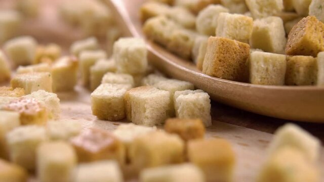 Crispy toasted bread croutons fall into a wooden spoon in slow motion. Cubes. Macro shot