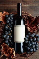 Bottle of red wine with grapes and dried vine leaves on an old wooden background.
