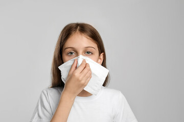 Little girl blowing nose into paper tissue on light grey background. Seasonal allergy