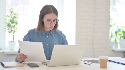 Fototapeta na wymiar Woman with Laptop Reading Documents in Office 