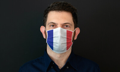 Man wearing French flag protective medical face mask. He looks worried and concerned. Coronavirus concept in France with black background.
